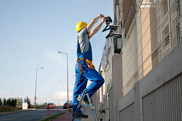 a technician installing a security camera system to the exterior of a building.