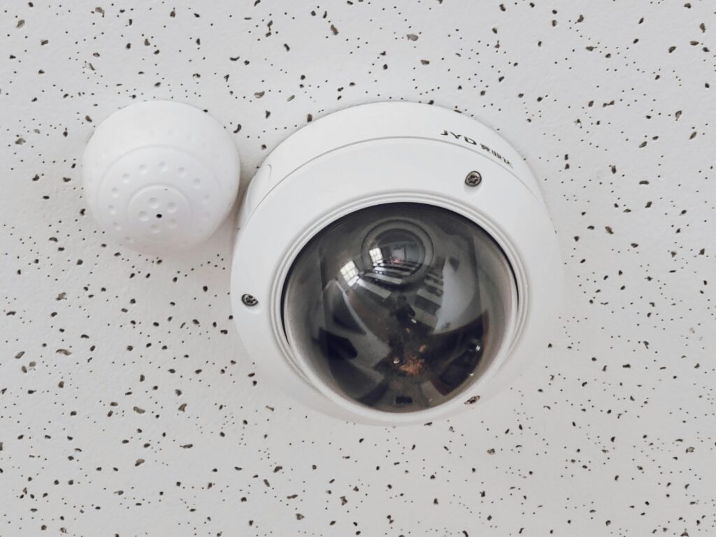 Close-up of a round dome surveillance camera installed on a speckled ceiling for security monitoring.